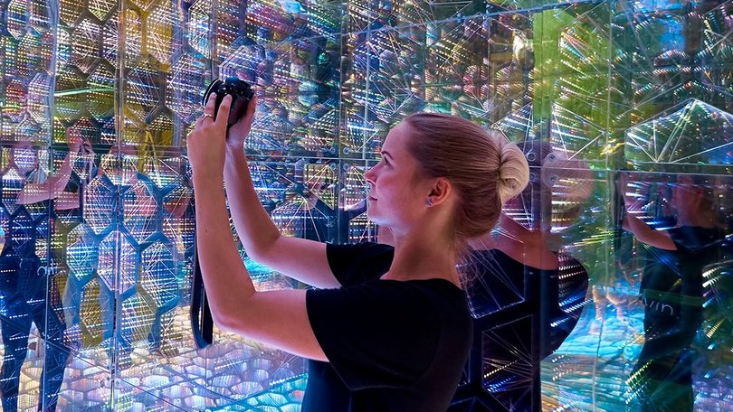 Frau fotografiert in einem mit Spiegeln und bunten Lichtern gestalteten Raum, ein Beispiel für immersive Erlebnisse auf Messen.